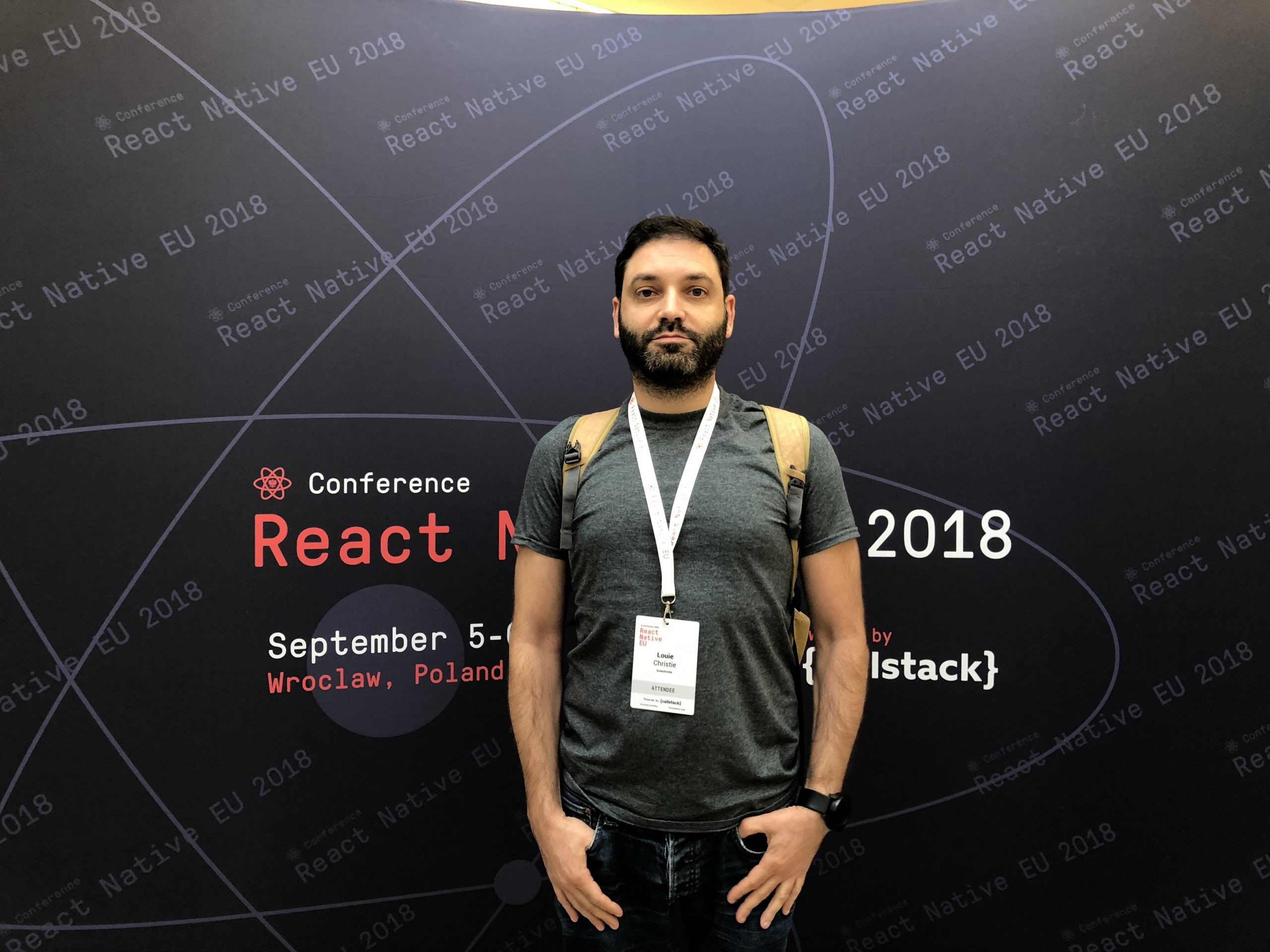 Louie Christie standing in from of a banner about the React Native conference 2018